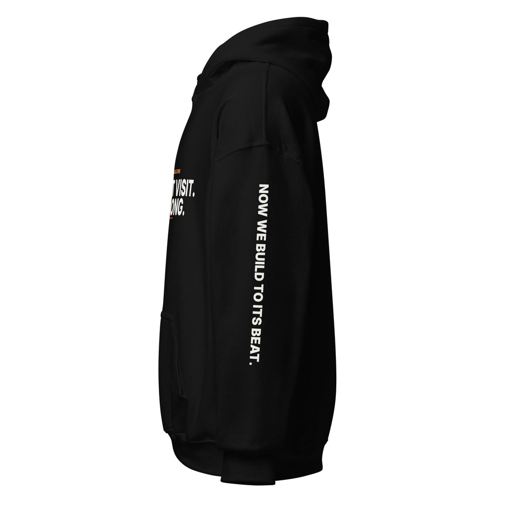 Right sleeve of the black Lesson 05 hoodie, printed with ‘Now We Build to Its Beat.’ in white.
